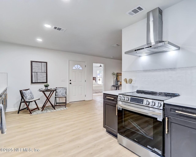 kitchen with wall chimney range hood, backsplash, stainless steel range with electric cooktop, and light wood-type flooring