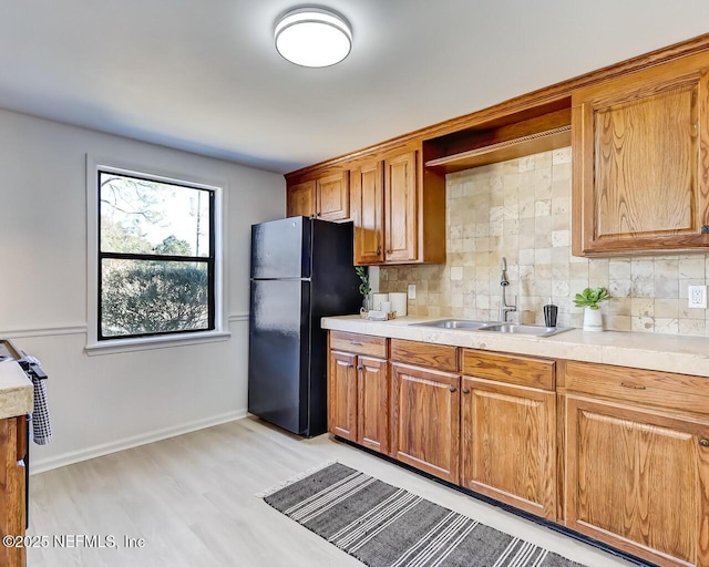 kitchen featuring black refrigerator, light hardwood / wood-style floors, sink, and backsplash