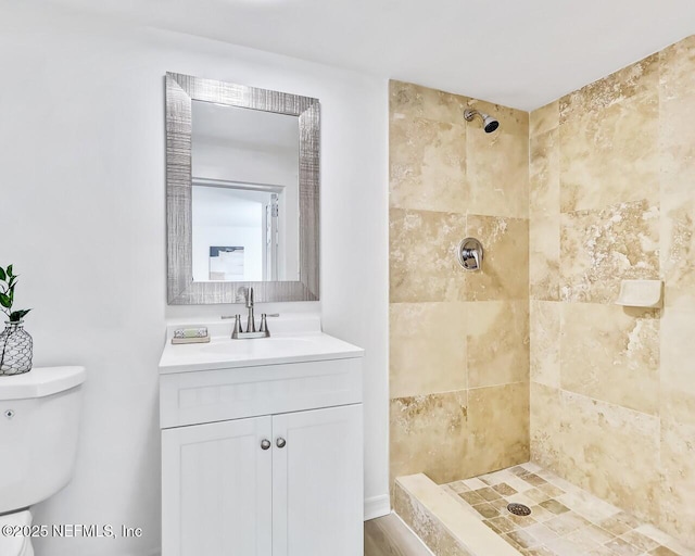 bathroom featuring a tile shower, vanity, and toilet