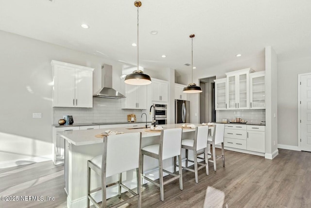 kitchen with white cabinetry, decorative light fixtures, wall chimney exhaust hood, and appliances with stainless steel finishes