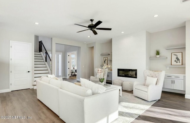 living room featuring ceiling fan, a large fireplace, and light hardwood / wood-style floors