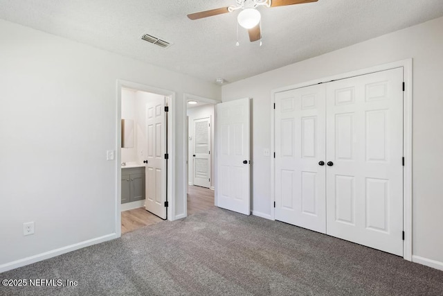 unfurnished bedroom with ensuite bathroom, light carpet, a textured ceiling, a closet, and ceiling fan