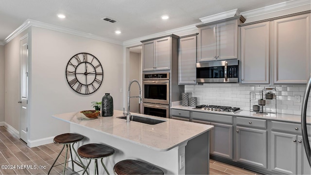 kitchen featuring stainless steel appliances, gray cabinets, and a center island with sink