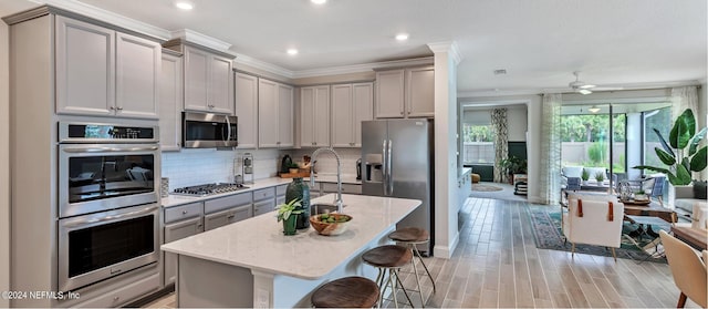 kitchen featuring a kitchen bar, gray cabinetry, light stone counters, a center island with sink, and appliances with stainless steel finishes