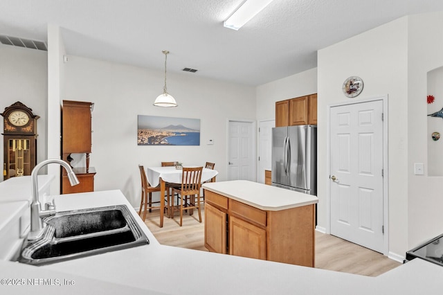 kitchen featuring sink, a center island, hanging light fixtures, stainless steel fridge, and light hardwood / wood-style floors