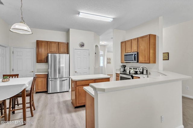 kitchen featuring stainless steel appliances, a kitchen island, decorative light fixtures, kitchen peninsula, and light wood-type flooring