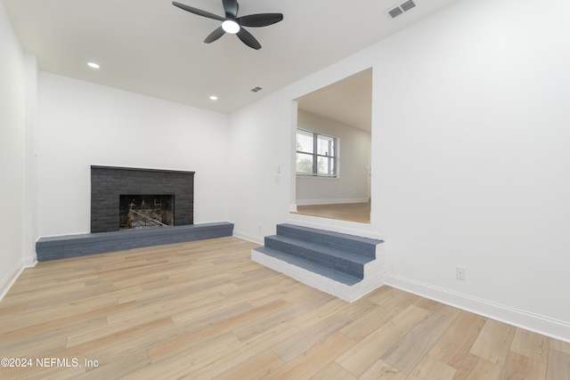 unfurnished living room featuring a brick fireplace, ceiling fan, and light hardwood / wood-style flooring