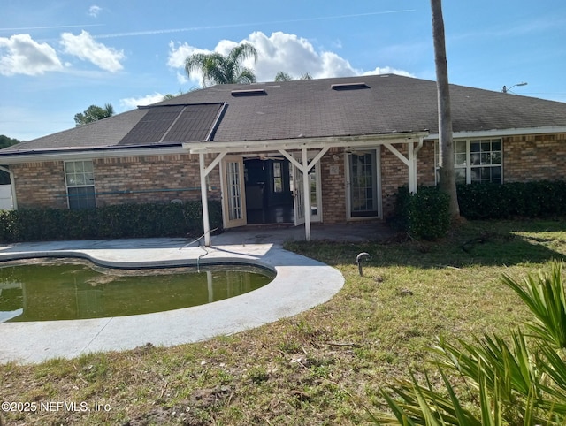 rear view of property featuring a lawn, a patio, and solar panels