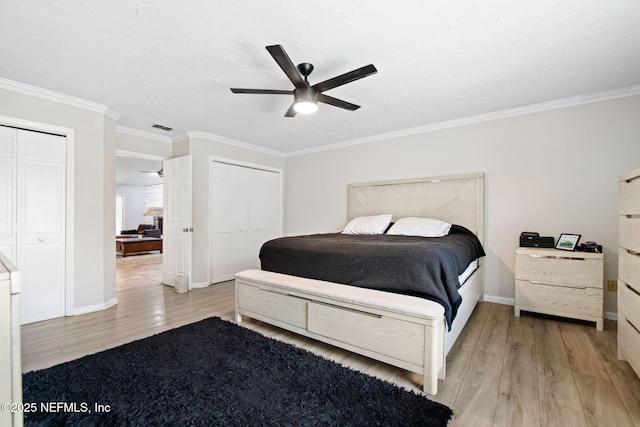 bedroom featuring crown molding, multiple closets, visible vents, light wood-type flooring, and baseboards