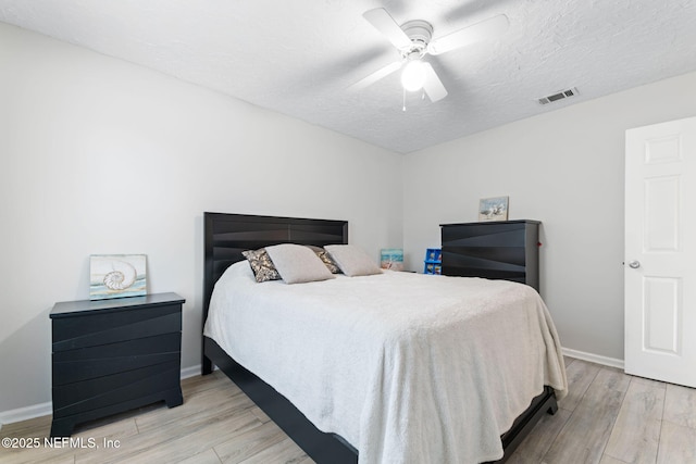 bedroom with baseboards, visible vents, a ceiling fan, wood finished floors, and a textured ceiling