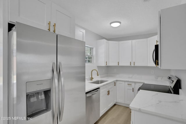 kitchen with sink, white cabinetry, stainless steel appliances, light stone countertops, and a textured ceiling