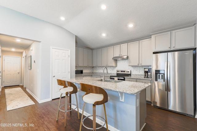 kitchen with vaulted ceiling, sink, a kitchen island with sink, light stone counters, and stainless steel appliances