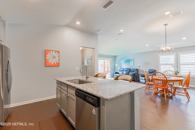 kitchen with pendant lighting, sink, appliances with stainless steel finishes, dark hardwood / wood-style floors, and a center island with sink