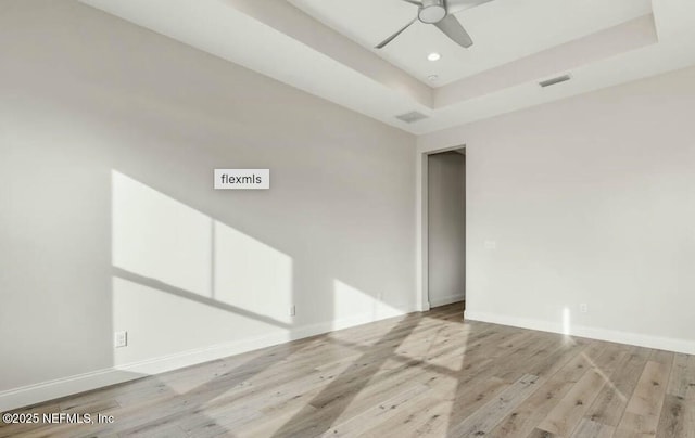 empty room featuring a raised ceiling, ceiling fan, and light wood-type flooring