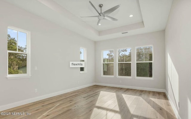 empty room featuring a raised ceiling, ceiling fan, a healthy amount of sunlight, and light hardwood / wood-style floors