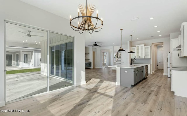 kitchen with white cabinetry, an island with sink, sink, dishwasher, and hanging light fixtures