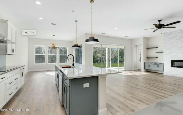 kitchen with sink, hanging light fixtures, gray cabinets, an island with sink, and white cabinets