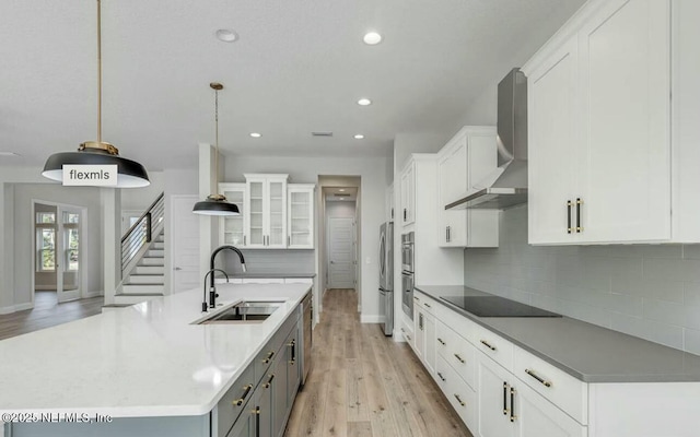 kitchen featuring decorative light fixtures, sink, white cabinets, stainless steel appliances, and wall chimney range hood