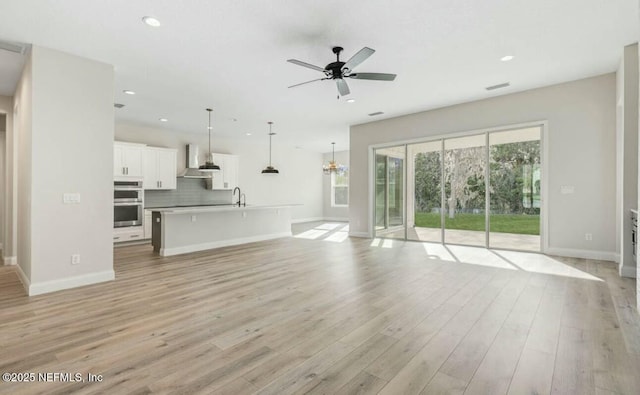 unfurnished living room with sink, ceiling fan with notable chandelier, and light wood-type flooring