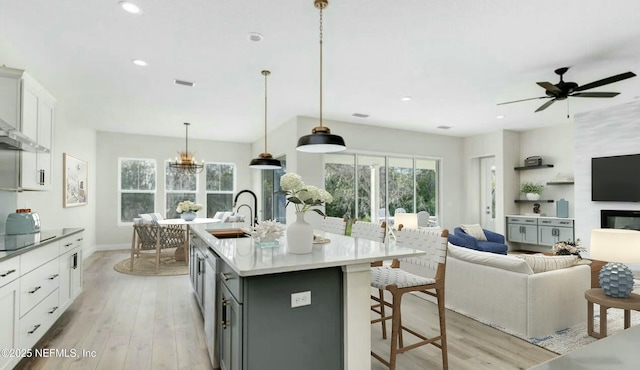 kitchen featuring decorative light fixtures, a breakfast bar area, gray cabinetry, white cabinets, and a center island with sink