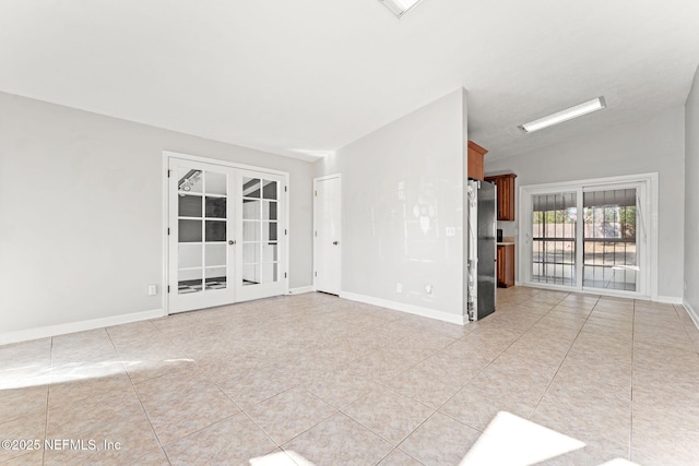 tiled empty room featuring vaulted ceiling and french doors