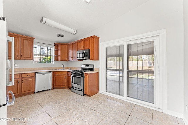 kitchen featuring sink, light tile patterned floors, vaulted ceiling, and appliances with stainless steel finishes