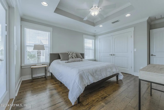 bedroom featuring ceiling fan, a raised ceiling, crown molding, dark wood-type flooring, and a closet