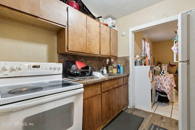 kitchen featuring sink, a textured ceiling, light wood-type flooring, white range with electric stovetop, and backsplash