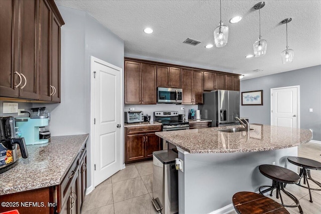 kitchen featuring a kitchen island with sink, hanging light fixtures, light stone counters, and stainless steel appliances