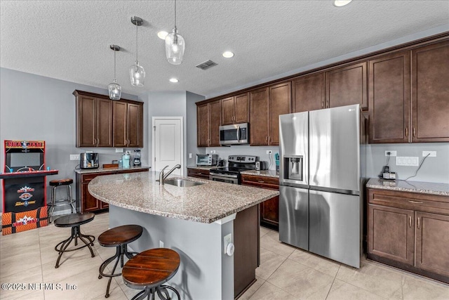 kitchen featuring decorative light fixtures, an island with sink, sink, a kitchen bar, and stainless steel appliances