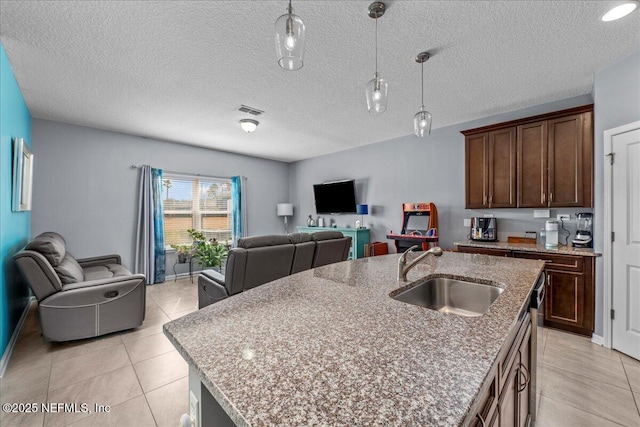 kitchen featuring sink, light tile patterned floors, a kitchen island with sink, hanging light fixtures, and light stone countertops