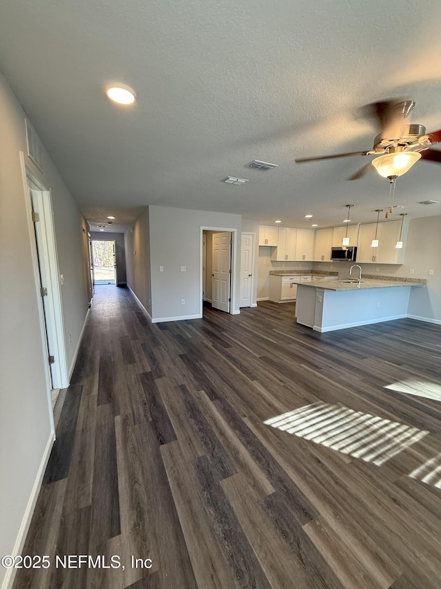 unfurnished living room with ceiling fan, sink, a textured ceiling, and dark hardwood / wood-style floors