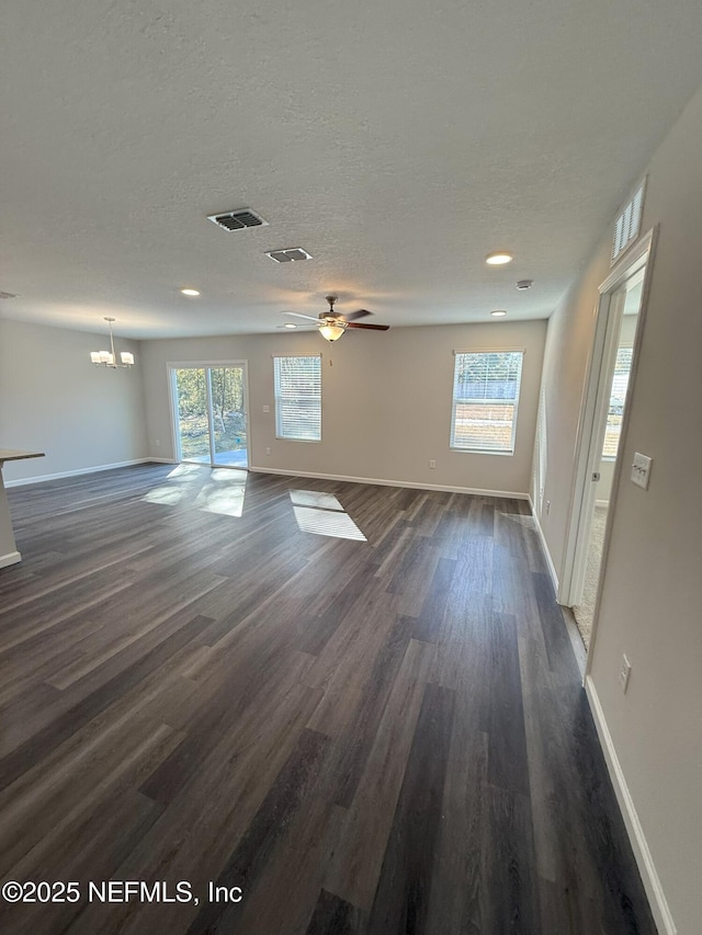 unfurnished living room featuring a healthy amount of sunlight, dark hardwood / wood-style flooring, ceiling fan with notable chandelier, and a textured ceiling