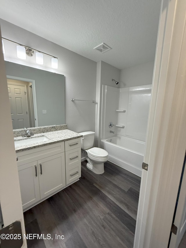 full bathroom with wood-type flooring, vanity, toilet, tub / shower combination, and a textured ceiling