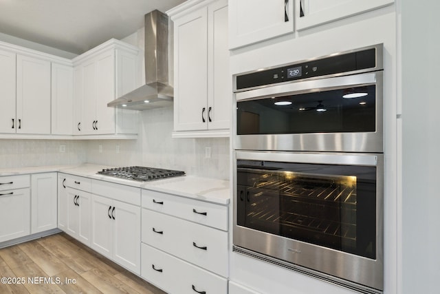 kitchen featuring white cabinets, decorative backsplash, light hardwood / wood-style floors, stainless steel appliances, and wall chimney exhaust hood