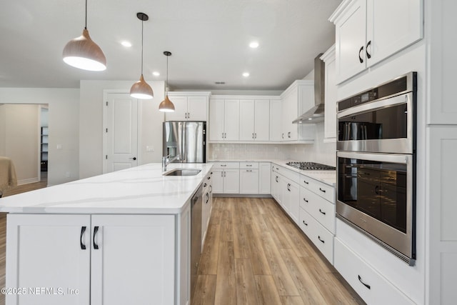 kitchen featuring a kitchen island with sink, wall chimney range hood, white cabinets, and appliances with stainless steel finishes