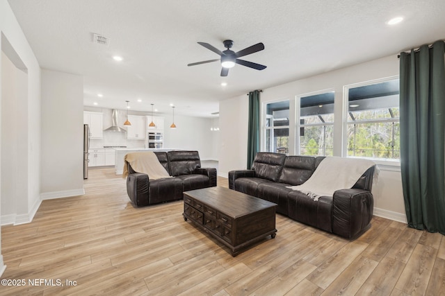 living room featuring ceiling fan, light hardwood / wood-style flooring, and a textured ceiling