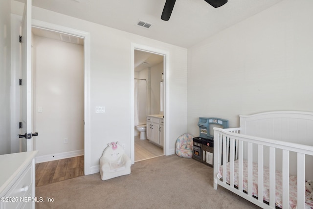 bedroom with connected bathroom, a crib, light colored carpet, and ceiling fan