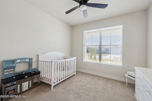 carpeted bedroom featuring a nursery area and ceiling fan