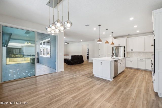 kitchen featuring white cabinetry, stainless steel appliances, light hardwood / wood-style floors, a center island with sink, and decorative light fixtures