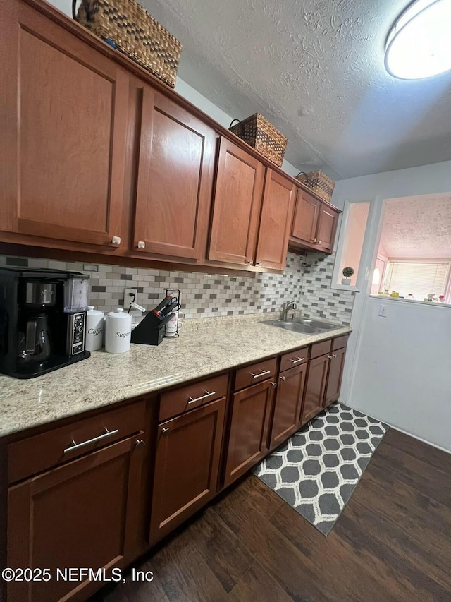 kitchen with sink, tasteful backsplash, a textured ceiling, dark hardwood / wood-style flooring, and light stone countertops