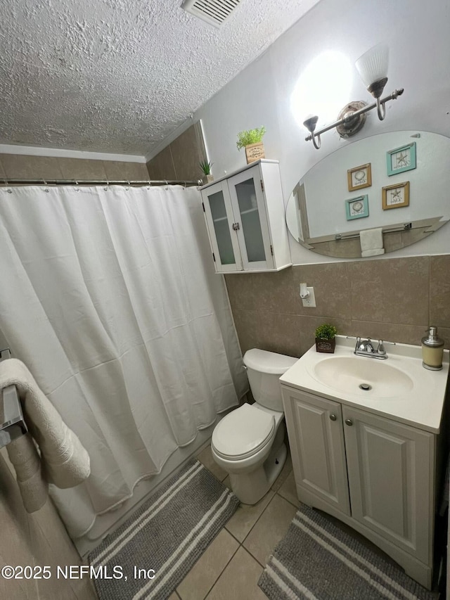 bathroom with tile walls, vanity, toilet, tile patterned floors, and a textured ceiling