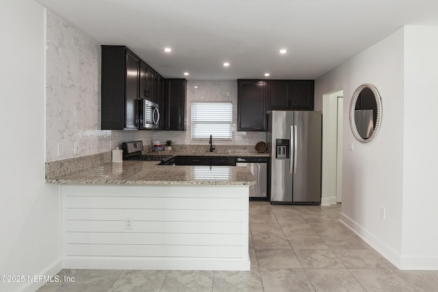 kitchen with sink, appliances with stainless steel finishes, kitchen peninsula, light stone countertops, and backsplash