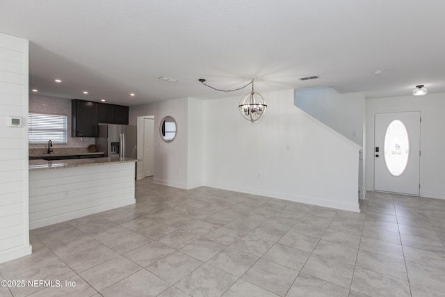 kitchen with sink, a chandelier, decorative backsplash, light stone counters, and stainless steel fridge with ice dispenser