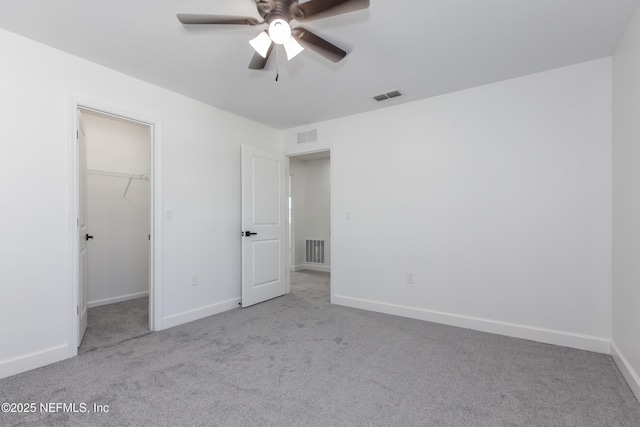 unfurnished bedroom featuring a walk in closet, light colored carpet, ceiling fan, and a closet