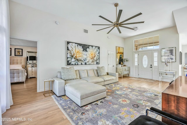 living room featuring ceiling fan, a towering ceiling, and light wood-type flooring