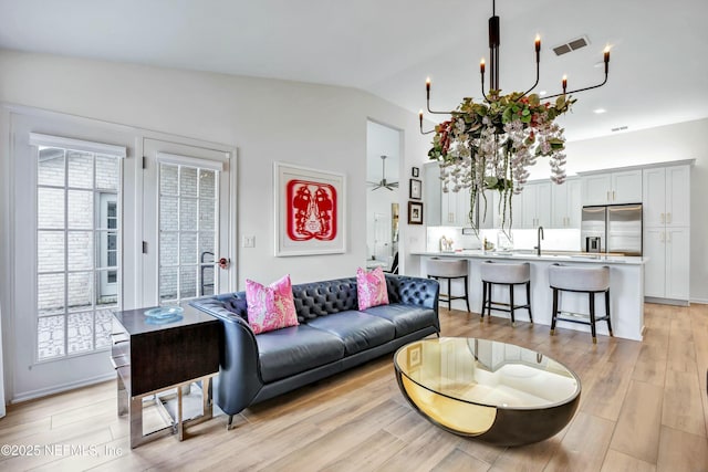 living room featuring an inviting chandelier, sink, vaulted ceiling, and light wood-type flooring