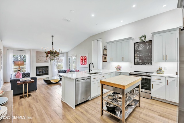 kitchen featuring sink, hanging light fixtures, stainless steel appliances, light hardwood / wood-style floors, and kitchen peninsula