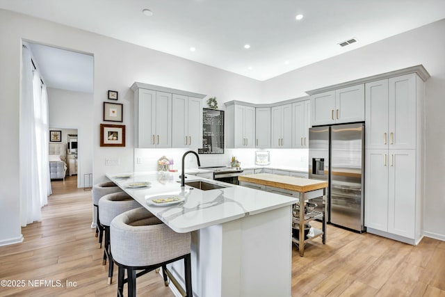 kitchen featuring stainless steel refrigerator with ice dispenser, sink, light stone counters, a kitchen breakfast bar, and kitchen peninsula