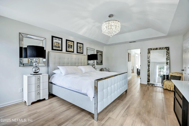 bedroom featuring a raised ceiling, a notable chandelier, and light hardwood / wood-style floors